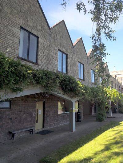 Vine-draped covered walkway beneath zigzag stone gables on a sunny school building.